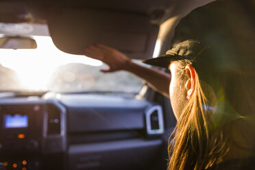 Beifahrerin auf dem Vordersitz eines Autos, die ihre Augen vor Sonnenlicht schützt, Blick über die Schulter - ISF21252
