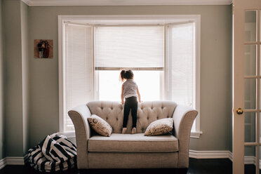 Mädchen steht auf dem Sofa und schaut durch das Wohnzimmerfenster, Rückansicht - ISF21281