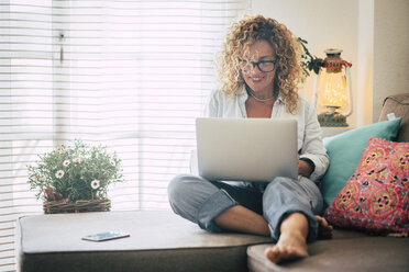 Smiling woman using laptop on couch at home - SIPF01945