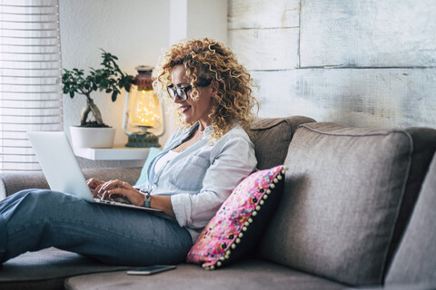 Smiling woman using laptop on couch at home stock photo