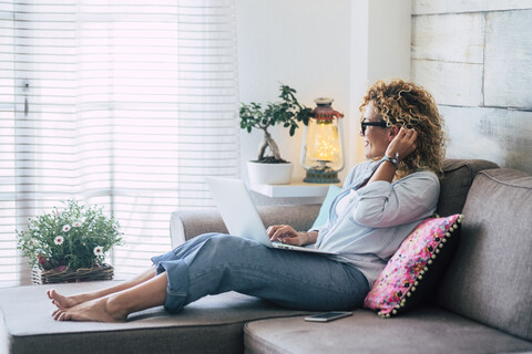 Frau benutzt Laptop auf der Couch zu Hause, lizenzfreies Stockfoto