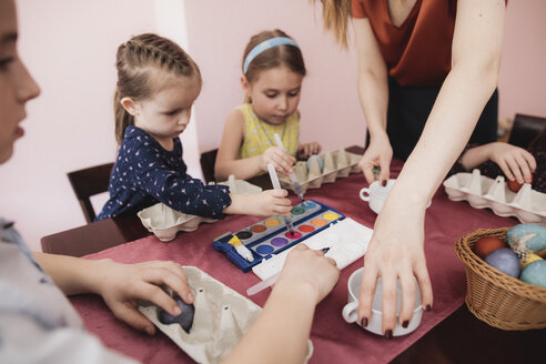 Mutter und Kinder bemalen Ostereier auf dem Tisch zu Hause - KMKF00925