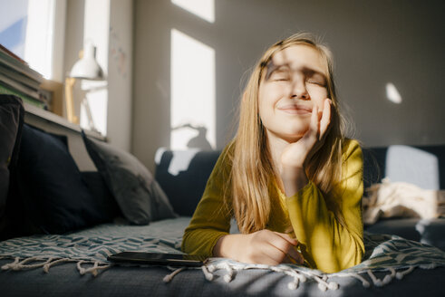 Mädchen auf der Couch zu Hause im Sonnenschein liegend - KNSF05832