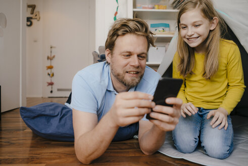 Vater und Tochter benutzen ein Mobiltelefon im Kinderzimmer - KNSF05846