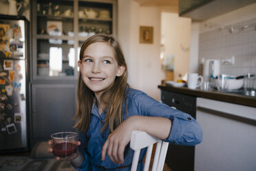 Glückliches Mädchen sitzt am Küchentisch zu Hause und hält ein Glas - KNSF05856