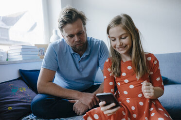 Vater und Tochter benutzen zu Hause ein Mobiltelefon - KNSF05873
