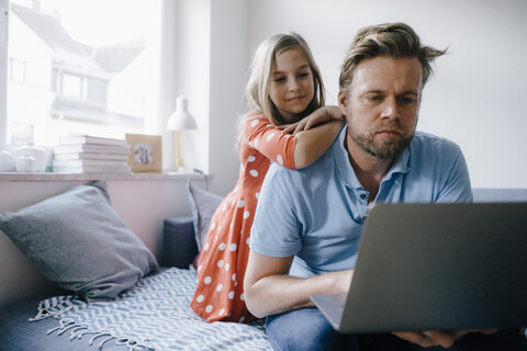 Girl watching father using laptop at home stock photo