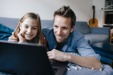 Glücklicher Vater und Tochter liegen auf der Couch zu Hause und benutzen einen Laptop - KNSF05886