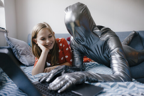 Mann im Morphsuit und Mädchen, das zu Hause auf der Couch liegt und einen Laptop benutzt, lizenzfreies Stockfoto