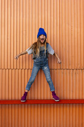 Young girl wearing dungarees, orange wall in the background - ERRF01256