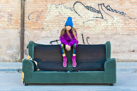 Mädchen trägt bunte Kleidung und sitzt auf einer Couch im Freien, lizenzfreies Stockfoto