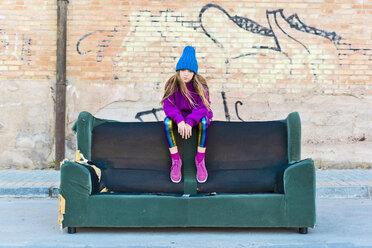 Girl wearing colorful clothing and sitting on a couch outdoors - ERRF01258