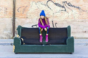Girl wearing colorful clothing and sitting on a couch outdoors - ERRF01260