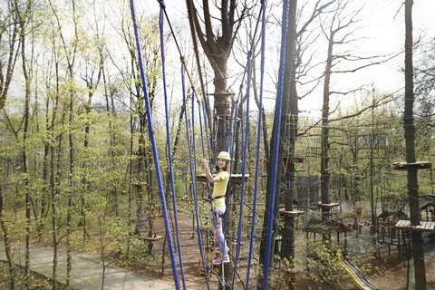 Junge Frau mit gelbem T-Shirt und Helm in einem Hochseilgarten, lizenzfreies Stockfoto