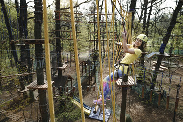 Young woman wearing yellow t-shirt and helmet in a rope course - EYAF00198