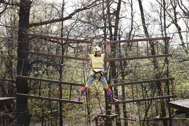 Junge Frau mit gelbem T-Shirt und Helm in einem Hochseilgarten - EYAF00199