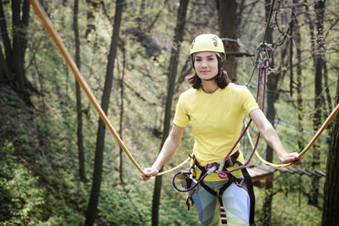 Junge Frau mit gelbem T-Shirt und Helm in einem Hochseilgarten - EYAF00207