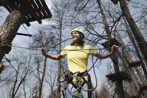 Junge Frau mit gelbem T-Shirt und Helm in einem Hochseilgarten - EYAF00210
