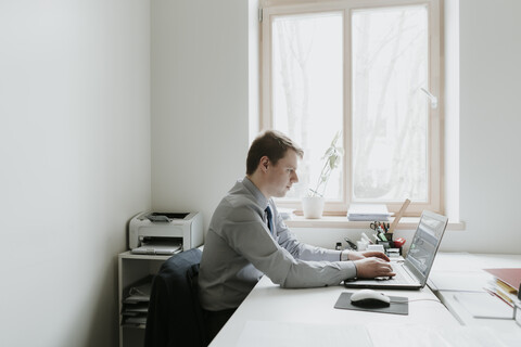 Junger Geschäftsmann mit Laptop am Schreibtisch im Büro, lizenzfreies Stockfoto