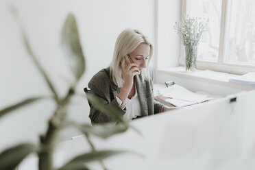 Junge Frau spricht am Schreibtisch im Büro mit einem Handy - AHSF00299