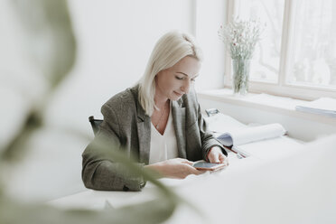 Young woman using cell phone at desk in office - AHSF00300