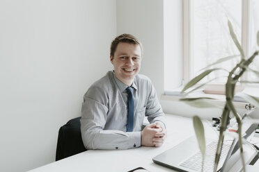 Porträt eines lächelnden jungen Geschäftsmannes, der am Schreibtisch im Büro sitzt - AHSF00301