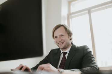 Lächelnder Geschäftsmann mit Computer am Schreibtisch im Büro - AHSF00323