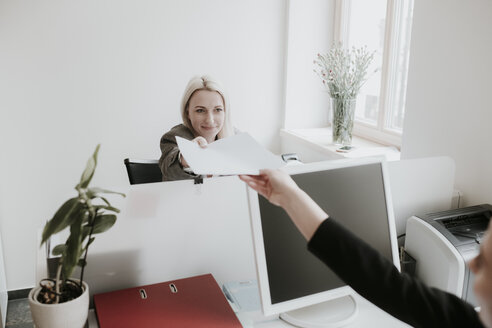 Zwei junge Frauen arbeiten am Schreibtisch im Büro und übergeben Papier - AHSF00334