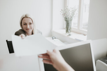 Zwei junge Frauen arbeiten am Schreibtisch im Büro und übergeben Papier - AHSF00335