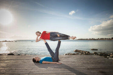 Women practising acro yoga at seaside - CUF50663
