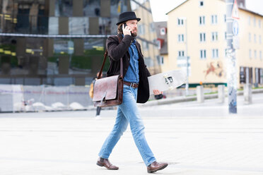 Männlicher Skateboarder, der auf einem Stadtplatz spazieren geht und mit seinem Smartphone telefoniert, Freiburg, Baden-Württemberg, Deutschland - CUF50838