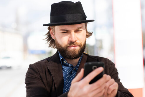 Mann mit Dreispitz schaut auf einer Straße in der Stadt auf sein Smartphone - CUF50842