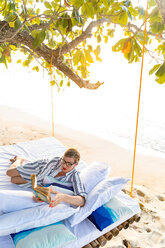 Frau, die auf einem Schaukelbett am Strand ein Buch liest, Insel Ginto, Linapacan, Philippinen - CUF51012
