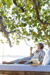 Frau, die auf einem Schaukelbett am Strand ein Buch liest, Insel Ginto, Linapacan, Philippinen - CUF51015