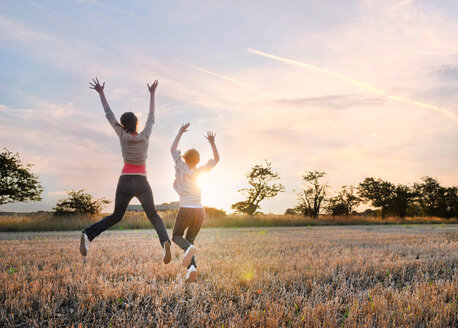 Girlfriends jumping in field, Southwold, Suffolk, Vereinigtes Königreich - CUF51036