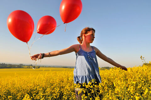 Mädchen mit roten Luftballons auf Rapsfeld, Eastbourne, East Sussex, Vereinigtes Königreich, lizenzfreies Stockfoto