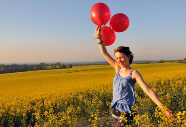 Mädchen mit roten Luftballons auf Rapsfeld, Eastbourne, East Sussex, Vereinigtes Königreich - CUF51039