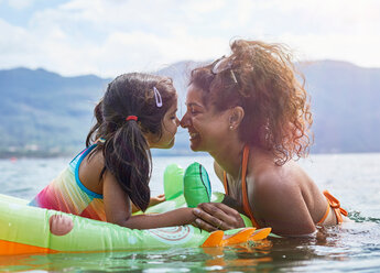 Mutter reibt sich mit Tochter auf aufblasbarem Frosch im See die Nasen - CUF51097