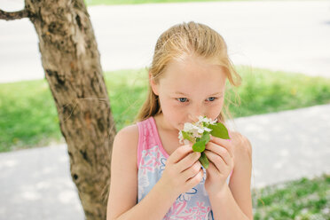 Girl smelling blossom on suburban street - ISF21302