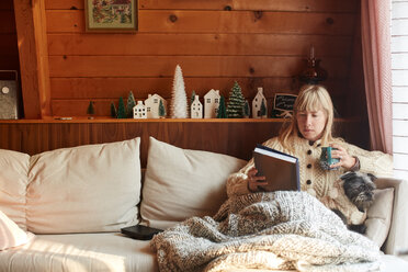 Frau liest Buch mit Hund auf Sofa zu Hause - ISF21327