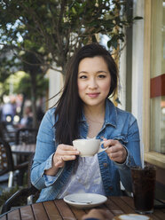 Lächelnde chinesische Frau trinkt Kaffee in einem Café im Freien - BLEF03065