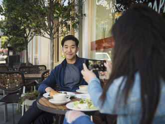 Chinesische Frau fotografiert Mann in einem Café mit Mobiltelefon - BLEF03067