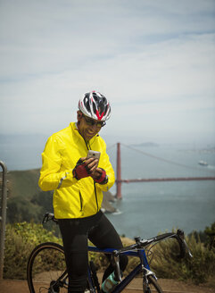 Hispanischer Mann auf dem Fahrrad, der am Hafen eine SMS mit seinem Handy schreibt - BLEF03070