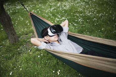 Gemischtrassiger Junge liegt in der Hängematte und trägt eine Virtual-Reality-Brille - BLEF03106