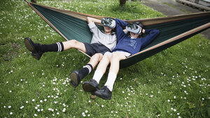 Mixed Race brother and sister in hammock wearing virtual reality goggles - BLEF03107