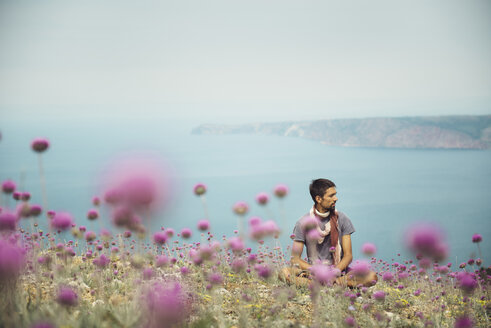 Caucasian man sitting in field of flowers near ocean - BLEF03122