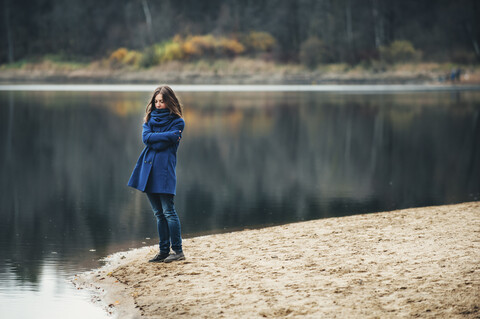 Kaukasische Frau mit blauem Mantel und Schal in der Nähe eines Sees, lizenzfreies Stockfoto