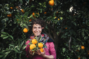 Smiling Caucasian woman holding oranges under tree - BLEF03152