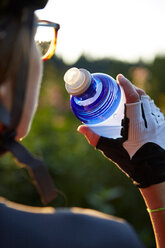 Radfahrerin, die aus einer Wasserflasche trinkt, Ausschnitt über die Schulter - CUF51175