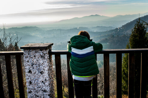 Junge, der vom Balkon aus auf eine Bergtallandschaft blickt, Rückansicht, Piani Resinelli, Lombardei, Italien - CUF51189